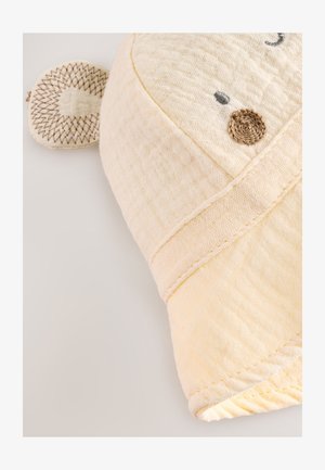 Prosop pentru bebeluși din muselină albă și moale, modelat ca o cap de animal, cu suprafață texturată, ochi brodați și o ureche decorativă.