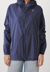 Námořnická lehká bunda s kapucí, strukturovaná tkanina, plný zip, elastické manžety a malá nášivka na hrudi. Volný střih.