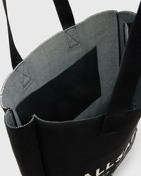Sac fourre-tout noir avec un extérieur en tissu texturé, doté de larges poignées et d'une poche intérieure. Le bord supérieur est roulé et cousu.