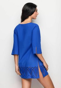 Túnica azul con mangas tres cuartos, un escote redondo y un intrincado detalle de cortes en el dobladillo y las aberturas laterales.