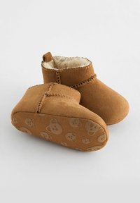 Bottines en daim marron doublées de fausse fourrure crème, avec une semelle en caoutchouc à motif de visages d'ours et une couture décorative le long des coutures.