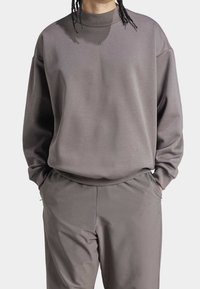 Tröja och byxor i en dämpad grå färg. Tröjan har en hög krage, avslappnad passform och en subtil logotyp på bröstet.