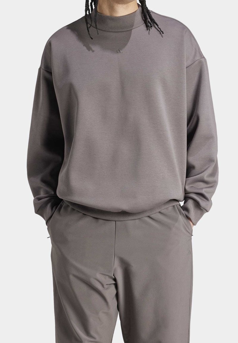 Tröja och byxor i en dämpad grå färg. Tröjan har en hög krage, avslappnad passform och en subtil logotyp på bröstet.