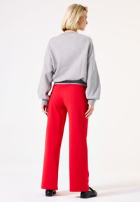 Sudadera gris de gran tamaño con puños acanalados, acompañada de pantalones rojos de pierna ancha y cintura alta. Tela suave y costuras planas visibles.