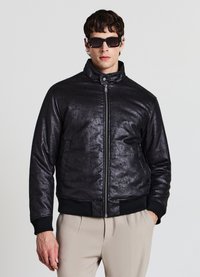 Schwarze Bomberjacke aus strukturiertem Material mit Reißverschluss, hohem Kragen sowie gerippten Bündchen an Ärmeln und Saum. Das Model trägt dunkle Sonnenbrillen.