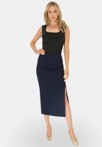 Czarny bezrękawnik w połączeniu z granatową, ołówkową spódnicą do kolan z bocznym rozcięciem. Modelka nosi beżowe szpilki. Gładki, dopasowany materiał.
