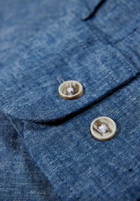 Tessuto di denim blu con un motivo texture, caratterizzato da due bottoni rotondi chiari con un design sottile su un colletto pieghettato.