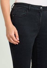 Zwarte denim jeans met een slim fit, voorzien van een voorkantzak, gestikte details en een metalen knoopaccent op de tailleband.