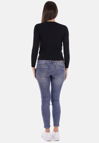 Top lungo a maniche nere a costine abbinato a jeans skinny blu chiaro. Presenta diverse tasche posteriori e una vita standard. Sneakers bianche.