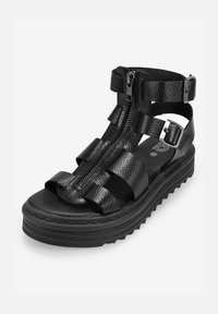 Sandal de plataforma negra con tiras de cuero, cierre de cremallera y acabado texturizado. El diseño incluye acentos en capas y una suela gruesa.
