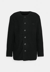 Schwarze Wolljacke mit rundem Halsausschnitt, sechs vorderen Knöpfen und zwei seitlichen Taschen, minimalistisches Design, dezentes "032c" Logo auf der Brust.