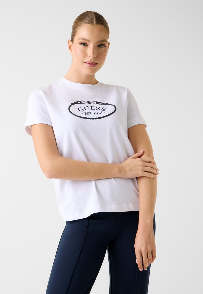 Weißes Baumwoll-T-Shirt mit rundem Ausschnitt, kurzen Ärmeln und einem schwarzen, gestickten "GUESS"-Logo mit "EST 1981" in einem ovalen Design.