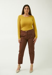 Maglia a maniche lunghe color senape, pantaloni a pieghe marroni con un bottone dorato e tacchi a punta scintillanti. Texture lisce e design aderente.