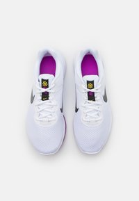 Scarpe da ginnastica bianche con una parte superiore in rete testurizzata. Presentano il famoso swoosh nero di Nike, soletta viola e dettagli decorativi neri e gialli.