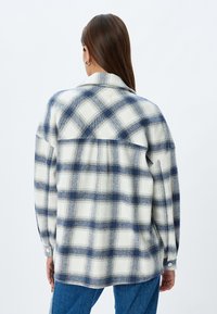 Camisa de franela a cuadros en beige y azul marino, con cuello, mangas largas y un corte holgado, con botones en los puños y un yugo en la espalda.