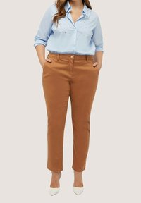 Chemise bleu clair à manches longues avec des embellissements, associée à un pantalon marron ajusté. La tenue présente un design épuré et une texture douce.