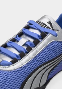 Κοντινό πλάνο μπλε και ασημί αθλητικού παπουτσιού Puma που δείχνει το πλέγμα στο πλάι, μπλε κορδόνια περασμένα από μαύρες τρυπούλες και το λογότυπο της μάρκας στη γλώσσα.