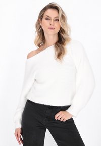 White, ribbed off-the-shoulder sweater with a soft texture, paired with black high-waisted jeans. The sweater features frayed hems.
