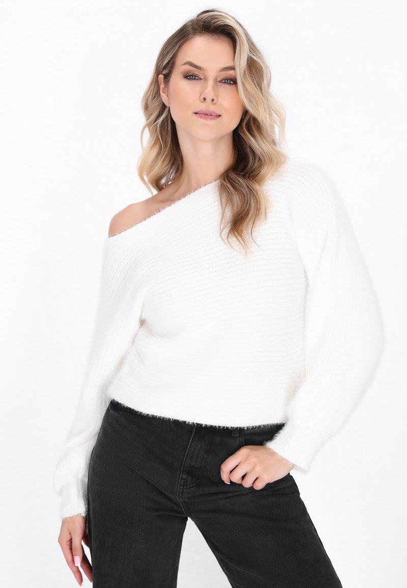 White, ribbed off-the-shoulder sweater with a soft texture, paired with black high-waisted jeans. The sweater features frayed hems.