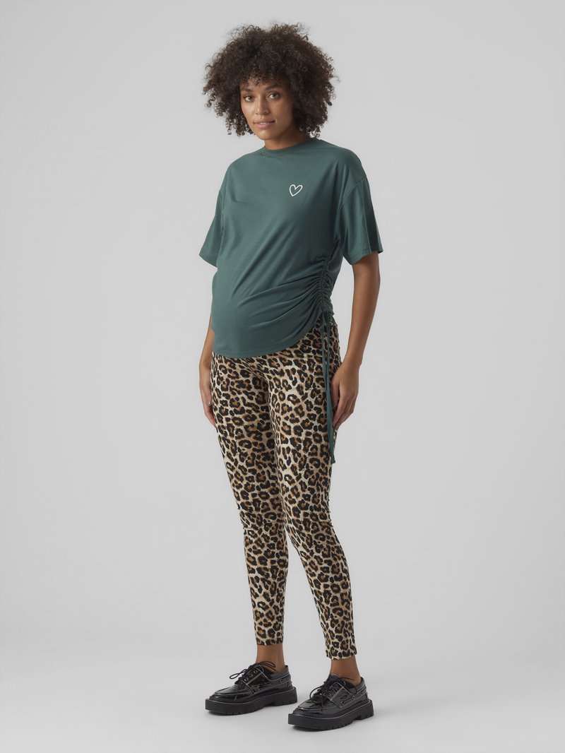 Umstandst-Shirt in Dunkelgrün mit kurzen Ärmeln und seitlicher Raffung, kombiniert mit Leggings im Leopardenmuster. Schwarze Plateauschuhe.