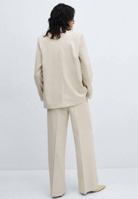 Béžový oversize blazer spárovaný s odpovídajícími širokými kalhotami, se hladkou texturou, minimálními švy a knoflíkovými detaily.