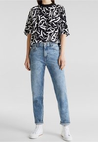 Haut à manches courtes noir et blanc avec un motif abstrait, associé à un jean bleu clair et à des baskets montantes blanches. Design minimaliste.