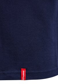 Granatowa tkanina o fakturze z małą czerwoną metką z białym napisem marki Hummel blisko brzegu.