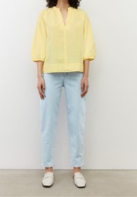 Żółta lniana bluzka z dekoltem w serek, luźny krój i bufiaste rękawy. Połączona z jasnoniebieskimi dżinsami o wysokim stanie i białymi butami wsuwanymi.