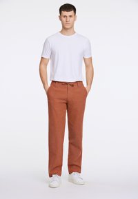 Roestkleurige linnen broek met een tailleband met trekkoord, gecombineerd met een eenvoudig wit T-shirt en witte sneakers. Eenvoudig ontwerp en ademend materiaal.