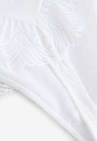 Lencería blanca con detalle de encaje intrincado y tela suave y lisa. El diseño incluye un borde festoneado y construcción sin costuras.