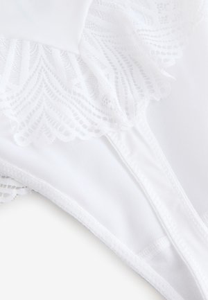 Baltas apakšveļas komplekts ar izsmalcinātu mežģīņu apdari un mīkstu, gludu audumu. Dizainā ir viļņota mala un bezšuvju konstrukcija.