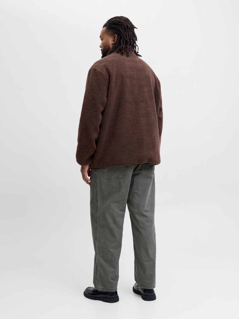 Chaqueta de forro polar marrón, diseño oversize, tejido texturizado. Combinada con pantalones holgados de color verde oliva y zapatos negros sin cordones. Fondo neutro.