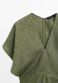 Abito verde oliva con scollo a V, realizzato in tessuto testurizzato. Presenta maniche corte e fluttuanti e una silhouette pulita e moderna.