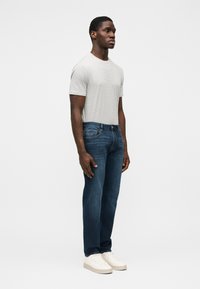 Camiseta gris de manga corta con un patrón texturizado, combinada con vaqueros de pierna recta azul oscuro y zapatillas blancas. Diseño simple, sin logotipos visibles.