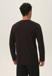 Czarna koszulka z długim rękawem wykonana z bawełny, z okrągłym dekoltem i luźnym krojem, pokazana z tyłu na neutralnym tle.