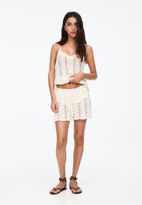 Crochet tank top and shorts set in cream, featuring a lace pattern, adjustable straps, and an elastic waistband with drawstring ties.