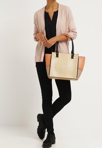 Bolso estructurado beige con asas negras, acentuado con paneles en melocotón y topo. El bolso presenta una superficie texturizada y un diseño elegante.