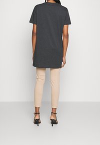 T-shirt gris au fit décontracté, à manches courtes et à col arrondi, associé à un pantalon beige clair ajusté et des talons noirs à lanières.