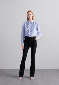 Light blue ruffled shirt with front buttons, paired with high-waisted black pants featuring side button accents. Simple, elegant design.