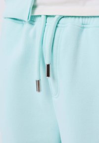 Pantaloni della tuta azzurri chiari con vita elastica e cordini abbinati con punte metalliche argentate.