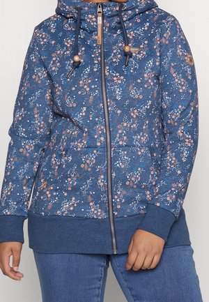 Blå hættetrøje med lynlås med lyserødt og hvidt blomsterprint, snore med træperler, båret med blå jeans, vist fra nakke til hofter.
