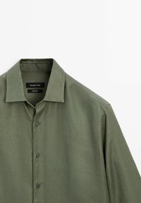 Oliwkowa lniana koszula z klasycznym kołnierzykiem, sześcioma guzikami z przodu i subtelną teksturą; wewnątrz kołnierza metka "Massimo Dutti".