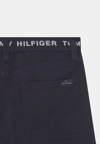 Ciemnogranatowe dżinsy z denimu z białym paskiem w talii z napisem "TOMMY HILFIGER", tylną kieszenią z charakterystyczną metką z logo.