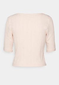 Jasnoróżowa, prążkowana bluzka z krótkim rękawem o szerokim dekolcie. Tkanina ma teksturowane wykończenie i jest dopasowana, kończąc się na wysokości talii.