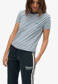 Striped t-shirt in cream and blue, featuring short sleeves and a round neckline. Paired with dark sweatpants displaying "SUPERDRY ATHLETIC."