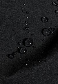 Tissu noir avec une surface texturée, présentant des gouttes d'eau de différentes tailles, indiquant une résistance à l'eau.