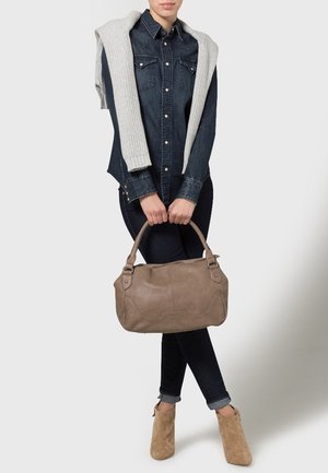 Lichtbruine leren handtas met een gladde textuur, voorzien van twee korte handvatten en een eenvoudige, ronde vorm. Casual denimoutfit gedragen met een trui.