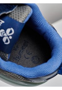 Intérieur de sneaker gris et bleu avec doublure en maille texturée, bords rembourrés et lettres discrètes sur une semelle intérieure foncée. Forme arrondie, sensation de coussin.