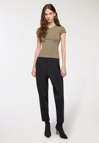 T-shirt aderente verde oliva a maniche corte abbinato a pantaloni neri a vita alta con gamba affusolata e stivaletti neri eleganti.