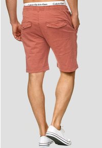 Shorts en terre cuite claire avec une texture légèrement rugueuse, dotés d'une taille élastique, de deux poches arrière et portés avec des baskets blanches.
